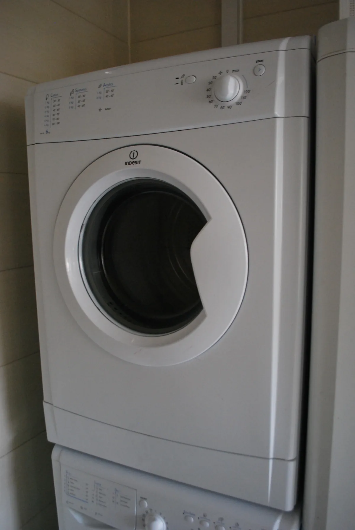 White front-load dryer stacked on a washer in a tiled corner